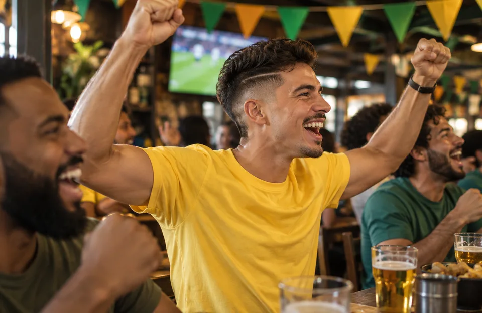 Cortes de cabelo da Copa do Mundo: torcedor com corte degradê e camisa amarela vibrando num bar durante o jogo